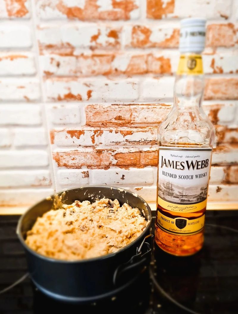Unbaked whiskey tea cake mixture in a round springform tin beside a bottle of Scotch whisky
