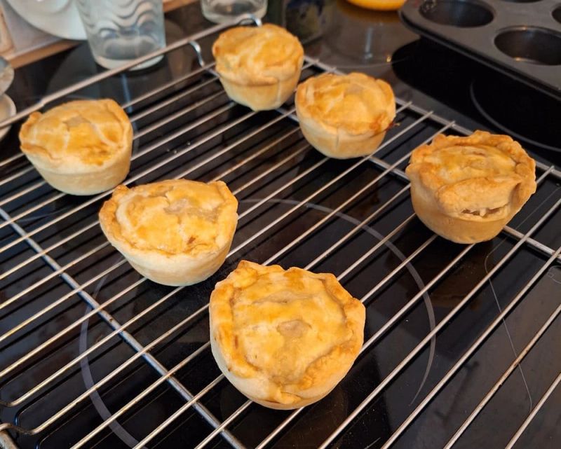Homemade mini pork pies with golden pastry cooling on a wire rack after baking.