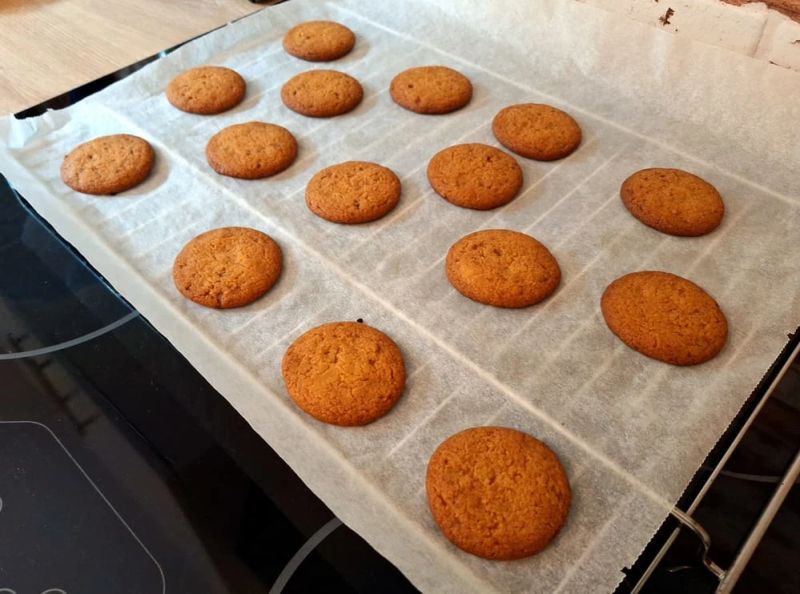 Freshly baked ginger nut biscuits cooling on a parchment-lined baking tray after being removed from the oven.