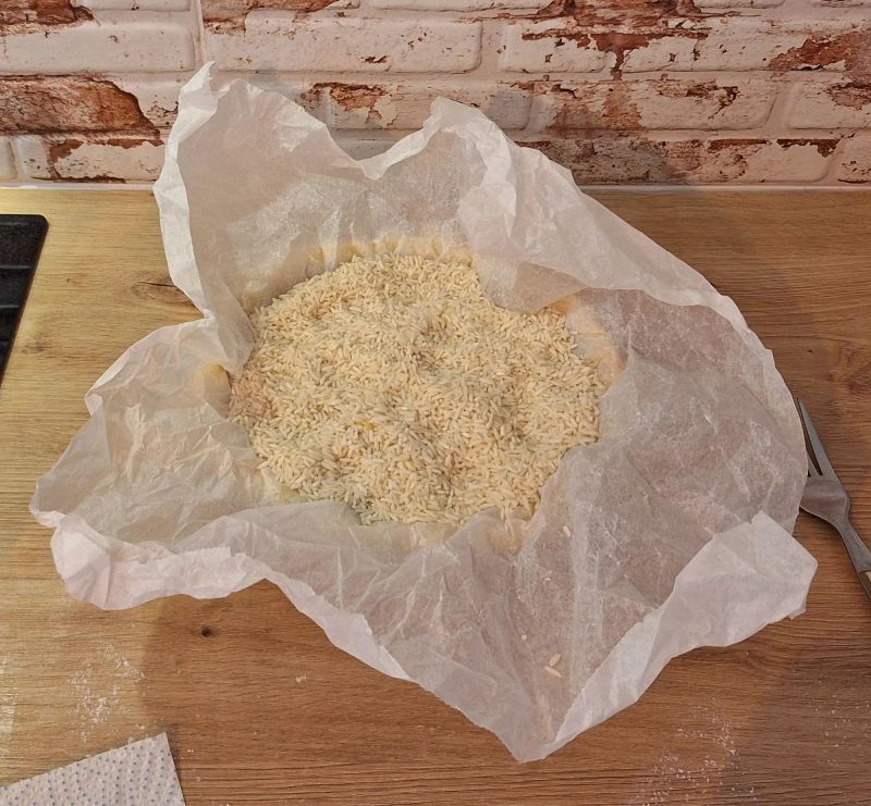 Shortcrust pastry lined with baking paper and uncooked rice ready for blind baking