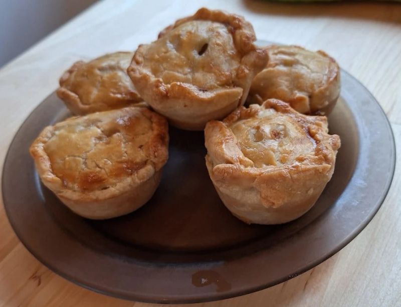 Homemade mini pork pies with golden hot water crust pastry stacked on a plate and ready to serve.