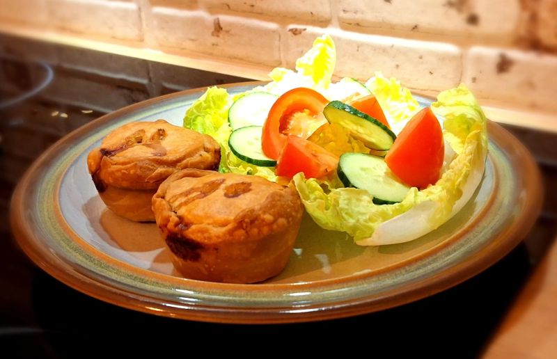 Homemade pork pies served with a side salad of lettuce, cucumber and tomato on a dinner plate.