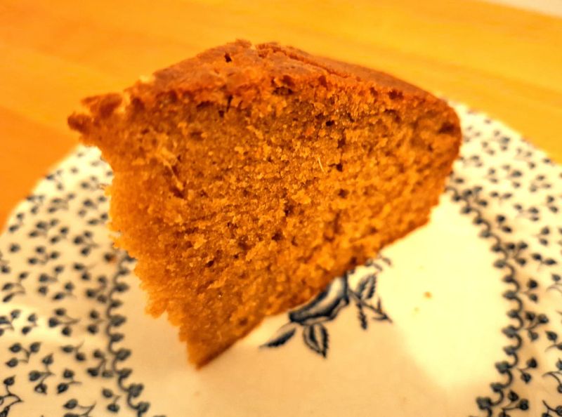 Slice of homemade ginger cake on a patterned plate, showing its moist texture and rich ginger crumb.