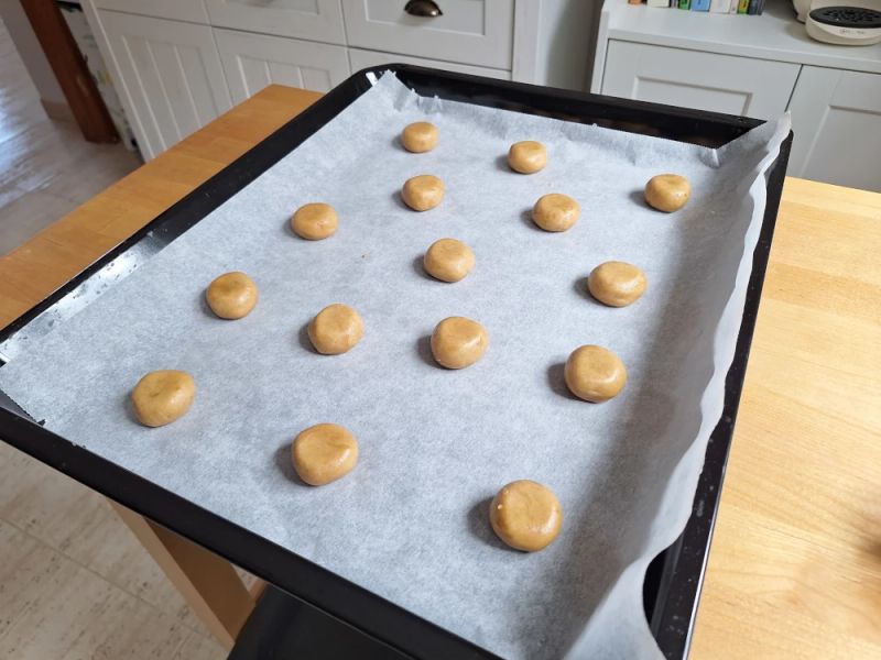 Ginger nut biscuit dough balls spaced on a parchment-lined baking tray ready for baking.