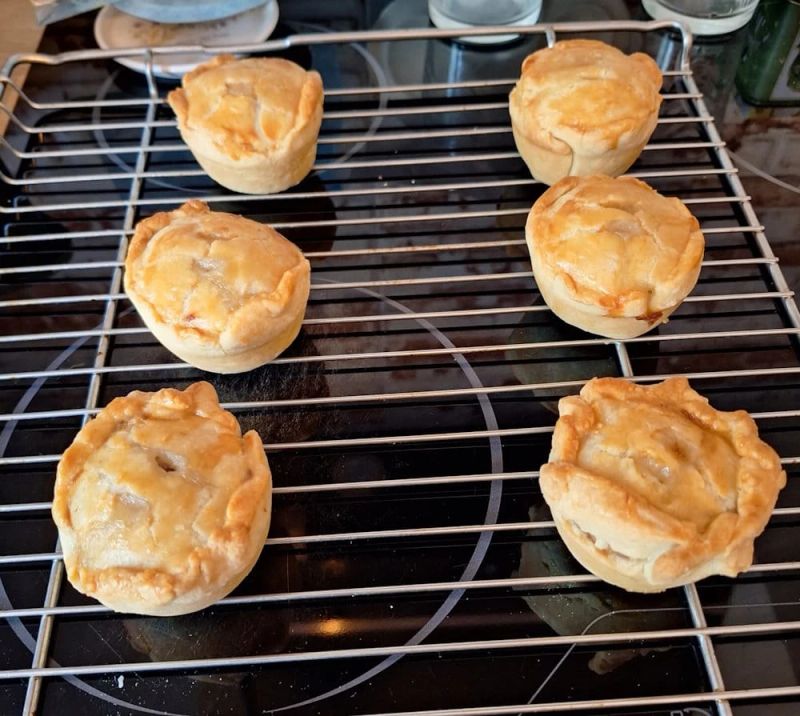 Freshly baked mini pork pies cooling on a wire rack after being removed from the oven.