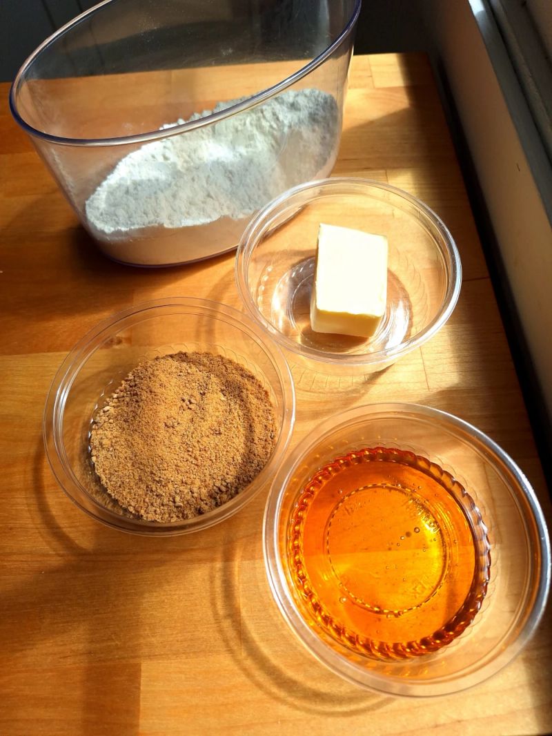 Flour, brown sugar, butter and golden syrup measured out in bowls ready to make ginger nut biscuits.