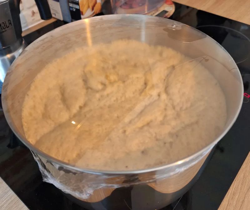 Hot cross bun dough rising in a covered mixing bowl during the first proof before shaping.
