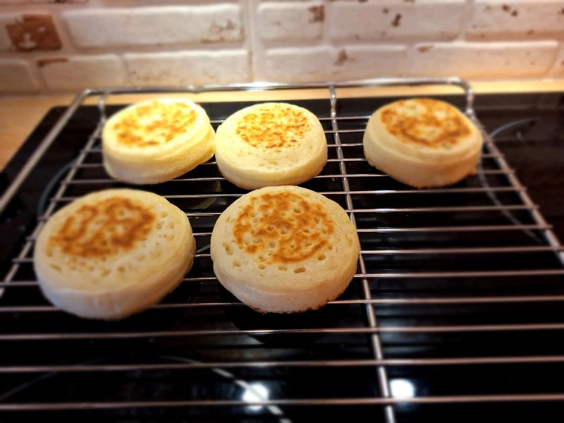 Five freshly cooked English crumpets cooling on a wire rack