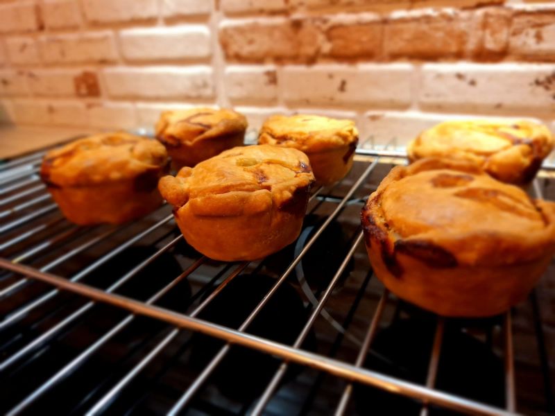 Freshly baked homemade pork pies cooling on a wire rack after being removed from the oven.