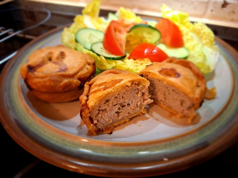 Homemade pork pie cut in half to reveal the seasoned pork filling, served with a fresh salad of lettuce, cucumber and tomato.