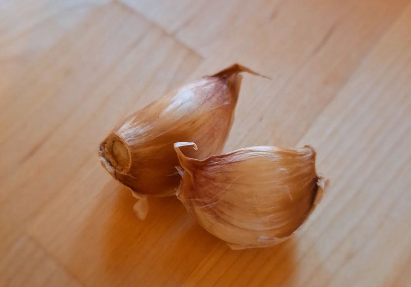 Two unpeeled garlic cloves on a wooden surface