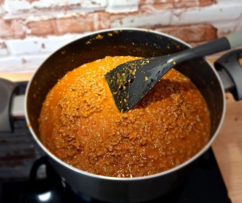 Ragù Bolognese simmering in a cooking pot with a slotted spoon